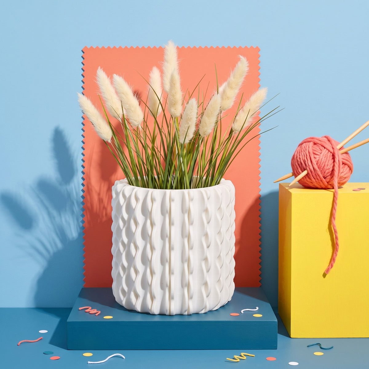 Trama bianco, porta vaso con texture a tessuto e coda di lepre, su set pop azzurro e corallo con gomitolo