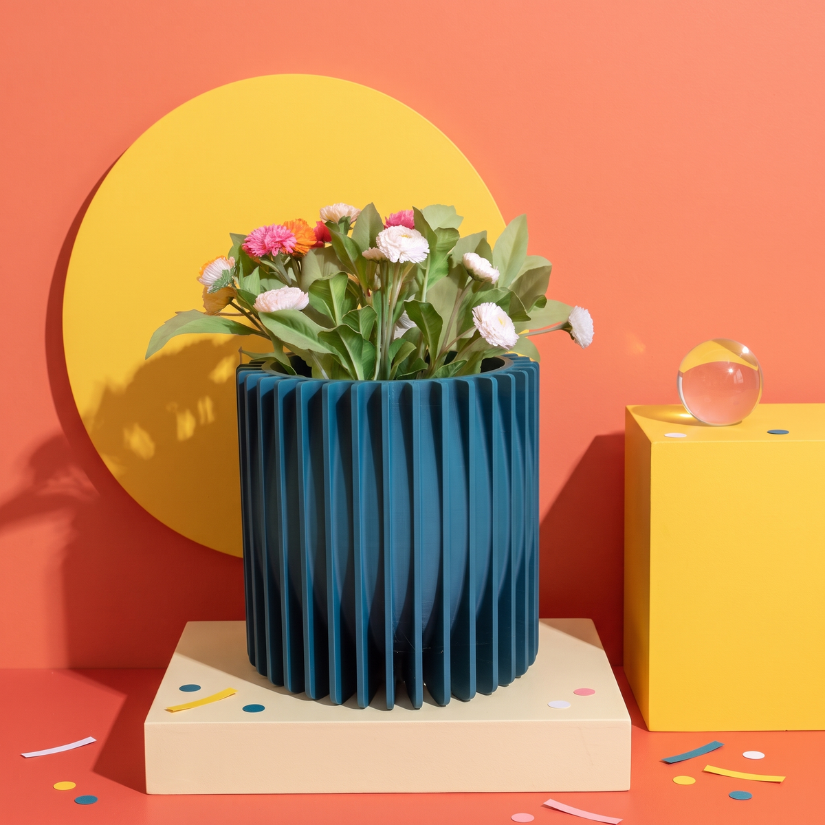 Riflesso petrolio, porta vaso a lamelle verticali con fiori, su set pop corallo e giallo con sfera di vetro
